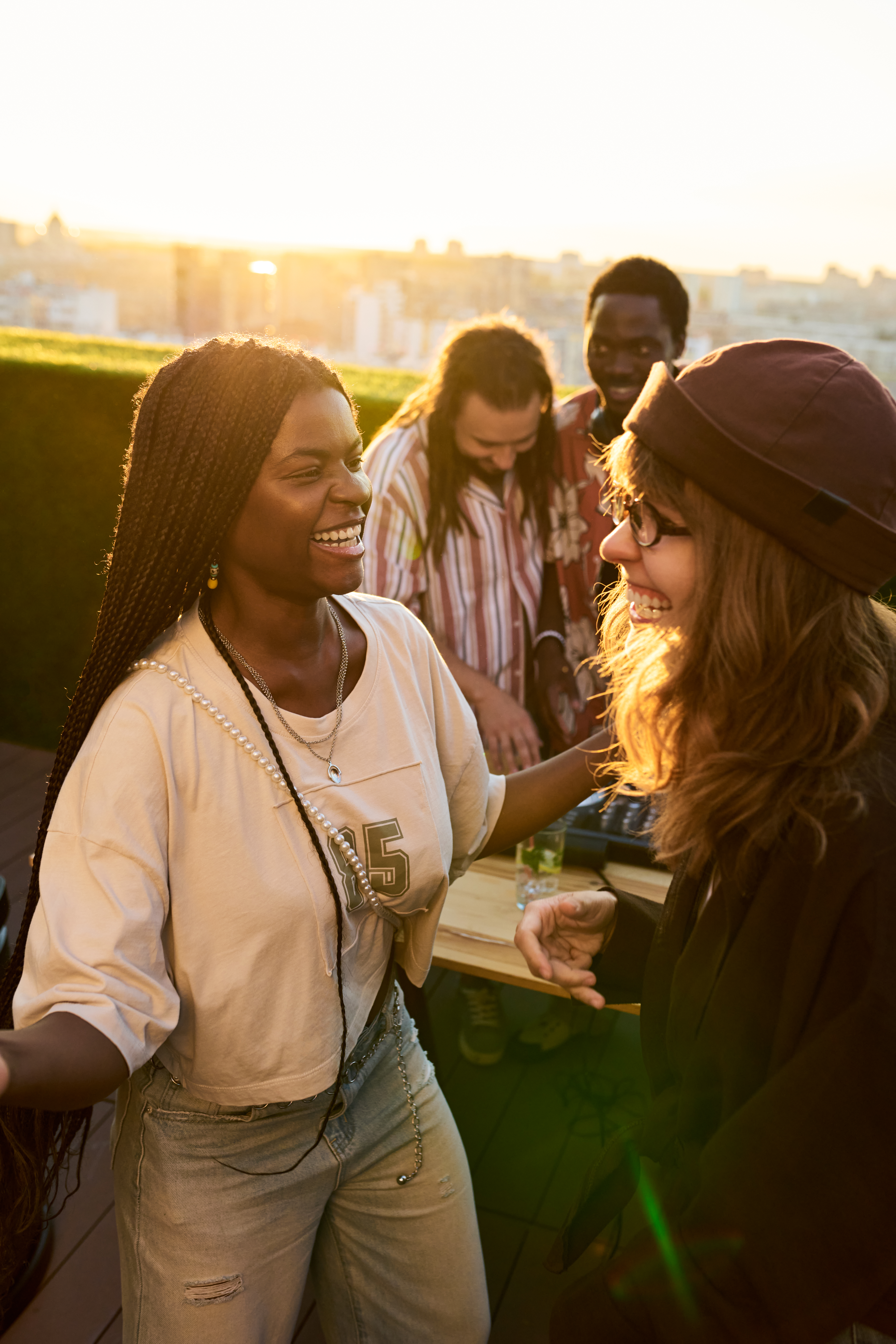 Vertical image of diverse young adults dancing, laughing at rooftop party. African American young woman, Caucasian friend enjoying leisure music for youth lifestyle campaigns